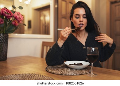 Beautiful female eating noodles with chopsticks and drinking red wine during dinner