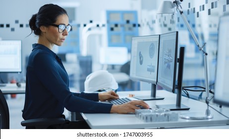 Beautiful Female Engineer Working On Personal Computer In The High-Tech Industrial Factory, She Uses CAD Software To Model Heavy Industry High Tech Mechanism 3D Model. Side View Shot