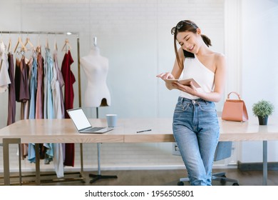 Beautiful Female Entrepreneur. Young cheerful Asian Woman fashion designer talking on mobile phone and checking notes in notebook. Startup Small business owner, Freelance work, SME marketing concept