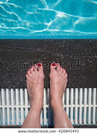 Beautiful female feet with red nail polish at the swimming pool