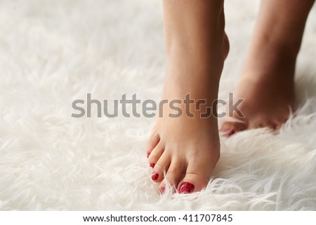 Beautiful female feet of white fake fur carpet