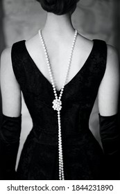 Beautiful female figure from the back in a black dress and pearls in the style of 20-30 years of the 20th century. Black and white photo - Shutterstock ID 1844231890