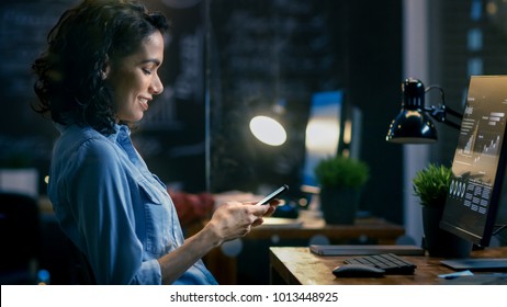 Beautiful Female Financier Uses Mobile Phone, Writing Messages, Emails while Smiling. In the Background Creative Office with Employees.