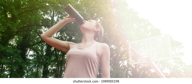 Beautiful Female Fitness Model Drinking Water After Workout Outside On A Sport Field