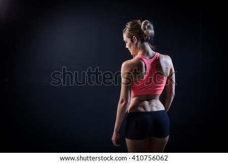 Rear view portrait of one young middle age athletic woman at crossfit training, exercising with trx suspension fitness straps over dark background