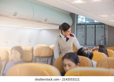 Beautiful female flight attendants checking the passengers on safety standard, seat belt, turn off electric devices, seat back and tray table in upright position before airplane take off and landing. - Shutterstock ID 2143553111
