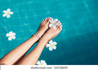 Beautiful female foot in swimming pool background with white Spa flowers