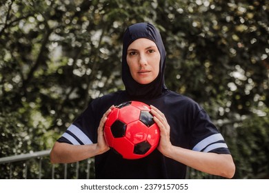 Beautiful female football player in hijab with ball in her hand. The woman plays soccer for relaxation. Concept of muslim woman in sport. - Powered by Shutterstock