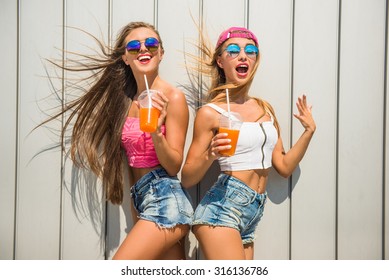 Beautiful female friends with juice are having fun against the wall, outdoor.