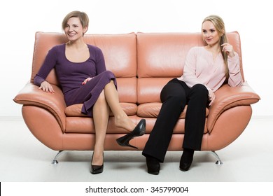 Beautiful Female Friends On The Sofa. Two Businesswomen. Body Language, Gestures Psychology. Paired Gestures. Female Gestures To Attract Men