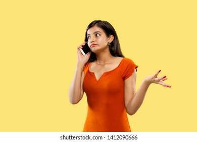 Beautiful Female Half-length Portrait Isolated On Yellow Studio Background. Young Emotional Indian Woman In Dress Talking On The Phone. Negative Space. Facial Expression, Human Emotions Concept.