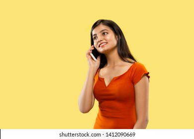 Beautiful Female Half-length Portrait Isolated On Yellow Studio Background. Young Emotional Indian Woman In Dress Talking On The Phone. Negative Space. Facial Expression, Human Emotions Concept.