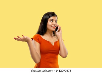 Beautiful Female Half-length Portrait Isolated On Yellow Studio Background. Young Emotional Indian Woman In Dress Talking On The Phone. Negative Space. Facial Expression, Human Emotions Concept.