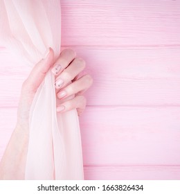 Beautiful Female Hand Holding Silk Fabric. Natural Manicure With Pink Color Nail Polish. Pale Pink Background. Copy Space