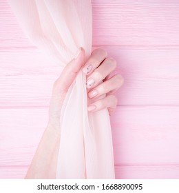 Beautiful Female Hand Holding Silk Fabric. Natural Manicure With Pink Color Nail Polish. Pale Pink Background. Copy Space