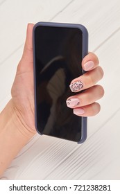 Beautiful female hand holding smartphone. Woman hands with gentle manicure holding mobile phone on white wooden background.