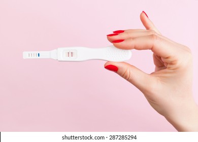 Beautiful female hand with red fingernails holding positive pregnancy test isolated on pink background. Motherhood, pregnancy, birth control concept. Minimal sparse modern image language. 