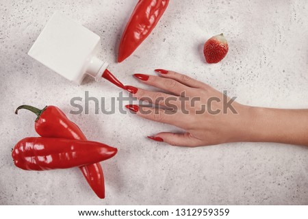 Beautiful female hand with red long manicure, white background, red hot pepper. Nail extension. Manicure, Spa salon. Creative, advertising.