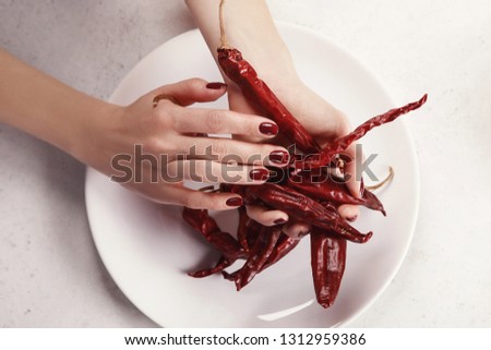 Beautiful female hands with dark red manicure, white background, red hot pepper on a plate. Nail extension. Manicure, Spa salon. Creative, advertising.