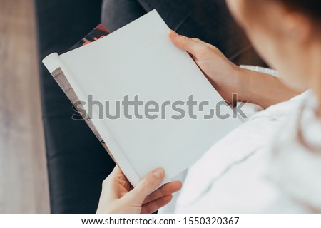 Beautiful female hands hold an open book or magazine in a room on a black sofa