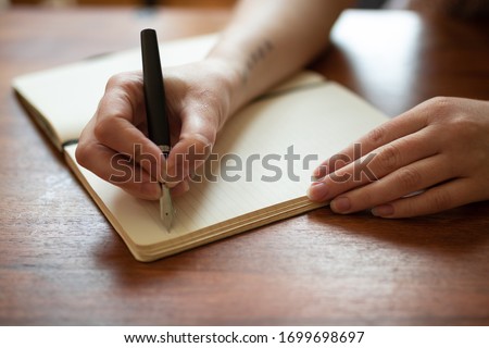 Beautiful female hands writing a journal entry in a diary using an ink fountain pen. 