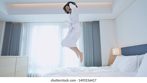 Beautiful Female Having Fun And Jumping With Bathrobe On Bed In Hotel Room