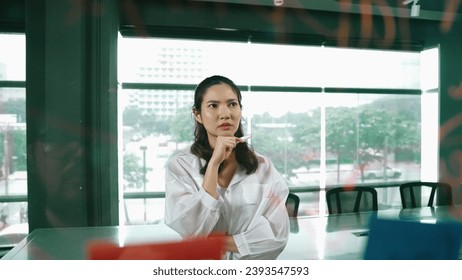 Beautiful female leader thinking about start up project in front of glass board. Smiling young project manager looking at colorful sticky notes with show creativity marketing strategy. Manipulator.