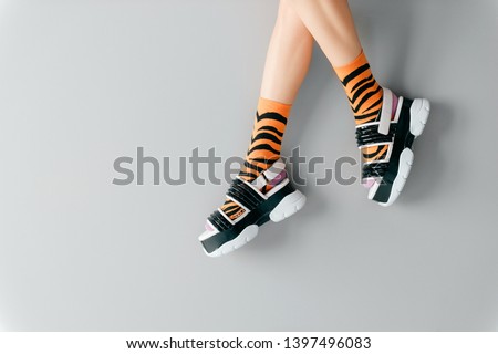 Beautiful female legs in striped orange trendy socks wearing fashionable black white high wedge leather sandals. Stylish womens footwear. Elegant girls legs in odd high sole shoes on gray background