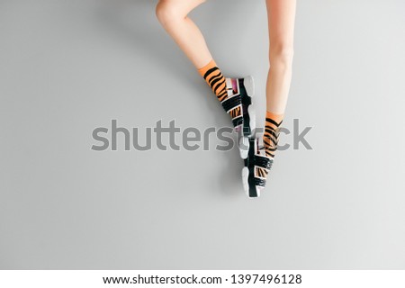 Beautiful female legs in striped orange trendy socks wearing fashionable black white high wedge leather sandals. Stylish womens footwear. Elegant girls legs in odd high sole shoes on gray background
