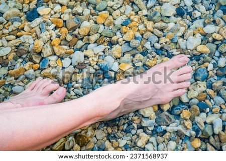 Beautiful female legs in the water of a lake with stones