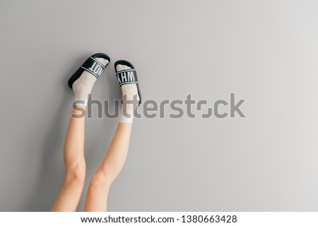 Beautiful female legs in white mesh teen socks wearing fashionable rubber slippers with inscroption why noton gray background. Elegant stylish trendy leg-wear . Voguish legwear for fashionable ladies