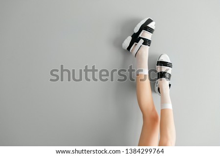 Beautiful female legs in white mesh trendy socks wearing fashionable black white high wedge leather sandals. Womens modern fashion footwear. Rebel girl in high sole stylish shoes on gray background