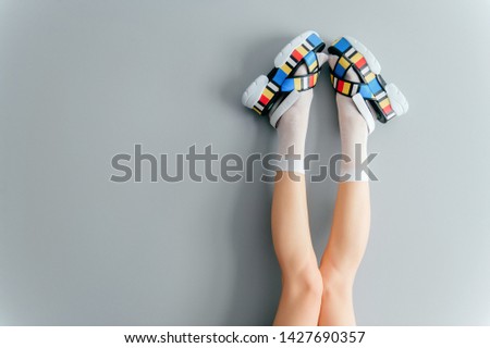 Beautiful female legs in white trendy socks posing in fashionable colorful high wedge leather sandals on gray background. Womens modern voguish footwear. Girl wearing high sole summer massive shoes.