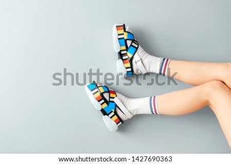 Beautiful female legs in white trendy socks posing in colorful fashionable high wedge leather sandals on gray background. Asian anime style concept. Womens legs wearing high sole summer stylish shoes