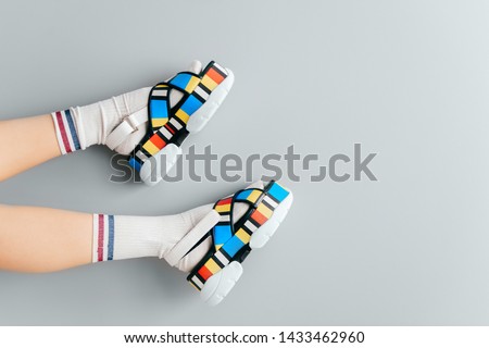 Beautiful female legs in white trendy socks posing in colorful fashionable high wedge leather sandals on gray background. Asian anime style concept. Womens legs wearing high sole summer stylish shoes
