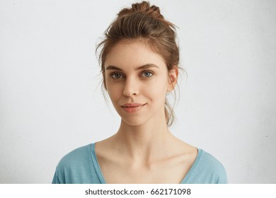 Beautiful Female With Lively Blue Eyes, Well-shaped Lips And Pure Skin Having Hair Bun Wearing Blue Casual Sweater Having Pleased Look. Sensual Young Woman With Appealing Face Looking Into Camera