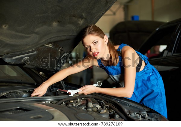 Beautiful\
female mechanic repairs the car with a\
wrench.