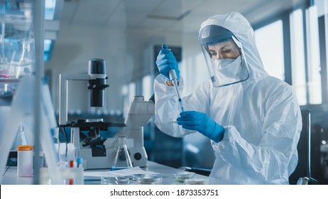 Beautiful Female Medical Scientist Wearing Coverall And Face Mask Using Micro Pipette While Working With Petri Dish. Vaccine, Drugs Research And Development Innovative Laboratory Modern Equipment