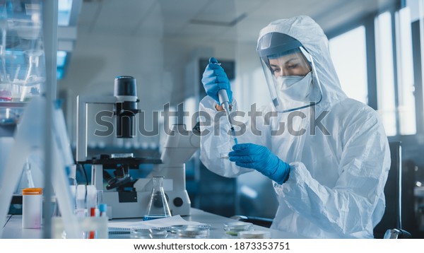 Beautiful Female Medical Scientist Wearing\
Coverall and Face Mask Using Micro Pipette while Working with Petri\
Dish. Vaccine, Drugs Research and Development Innovative Laboratory\
Modern Equipment