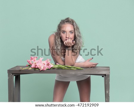 Beautiful female model standing at the table, on the table lay flowers. Green background. Blonde. Style.