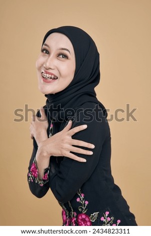 Beautiful female model wearing black batik kebaya, a traditional attire for Asian woman isolated over beige background. Stylish Muslim female hijab fashion lifestyle portraiture concept.