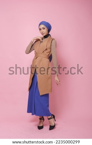 Beautiful female model wearing dark brown and blue colour dress with turban style hijab isolated over pink background. Stylish Muslim female hijab fashion lifestyle portraiture concept.