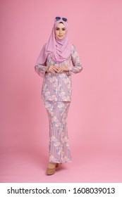 Beautiful female model wearing light pink batik design "baju kurung" with hijab, a modern lifestyle outfit  for Muslim woman isolated over pink background. Eidul fitri fashion and beauty concept.