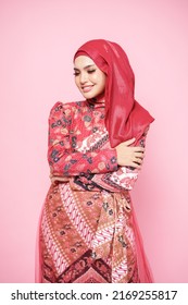 Beautiful female model wearing red batik kebaya with hijab, an Asian traditional dress for Muslim woman isolated over pink background. Stylish Muslim female fashion lifestyle  concept.