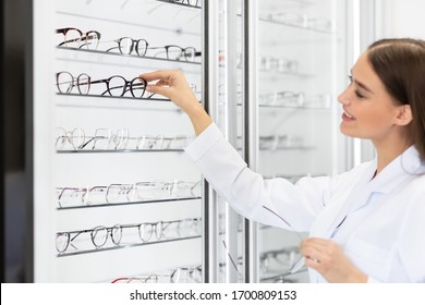 Beautiful female ophthalmologist seller choosing eyeglasses frame for her client in optical store, selective focus on hand