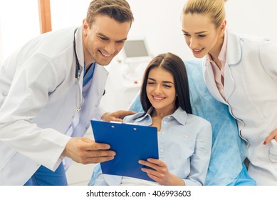 Beautiful Female Patient And Two Doctors Are Looking At Folder With Documents And Smiling, At The Doctors Office