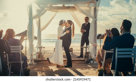 Beautiful Female Queer Couple Exchange Rings And Kiss At Outdoors Wedding Ceremony Near A Sea. Two Lesbian Women In Love Share Their Big Day With Diverse Multiethnic Friends. LGBTQ Relationship Goals.