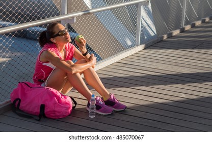 Beautiful Female Runner Resting And Eating An Apple On A Bridge