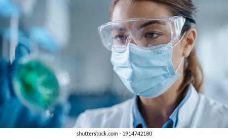 Beautiful Female Scientist Wearing Face Mask and Glasses Looking a Petri Dish with Genetically Modified Sample Chemicals. Microbiologist Working in Modern Laboratory with Technological Equipment.