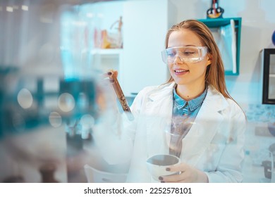 Beautiful Female Scientist Wearing Protective Goggles Mixing Chemicals in a Test Tube in a Lab. Young Professional Microbiologist Working in Modern Laboratory with Technological Equipment.